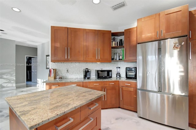 kitchen with black microwave, light stone counters, backsplash, freestanding refrigerator, and open shelves