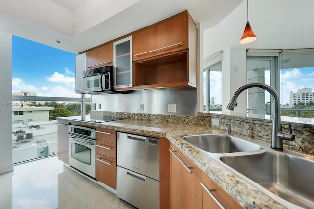 kitchen with pendant lighting, appliances with stainless steel finishes, glass insert cabinets, brown cabinetry, and a sink