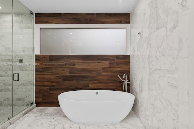 bathroom featuring a soaking tub, marble finish floor, stone wall, and a shower stall