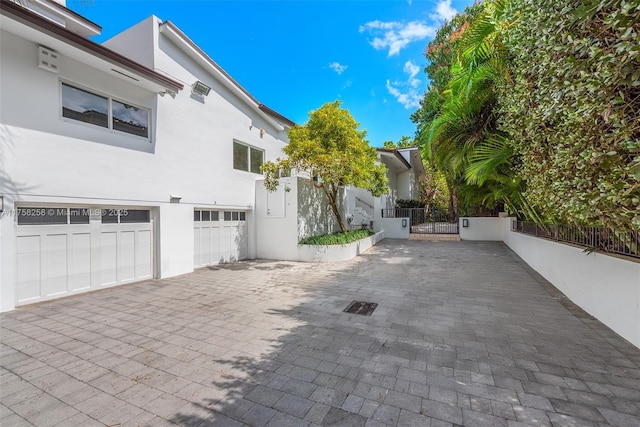 view of property exterior with stucco siding, an attached garage, decorative driveway, and fence