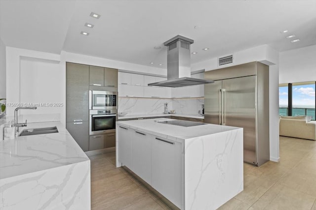 kitchen featuring built in appliances, island range hood, a sink, visible vents, and modern cabinets