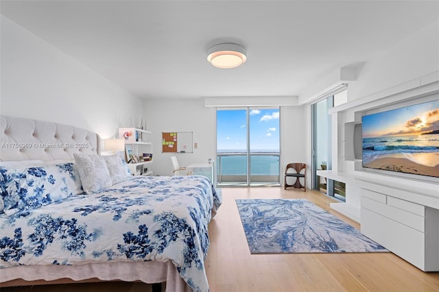 bedroom featuring access to exterior, a wall of windows, and wood finished floors