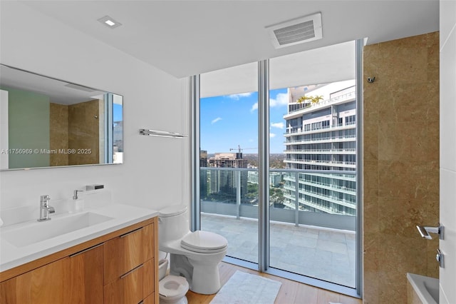 bathroom with toilet, a city view, vanity, visible vents, and floor to ceiling windows