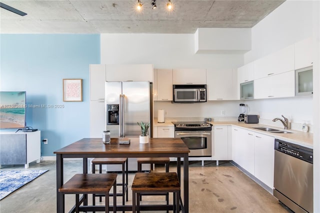 kitchen with stainless steel appliances, concrete floors, a sink, white cabinetry, and light countertops