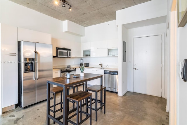 kitchen featuring finished concrete flooring, white cabinets, appliances with stainless steel finishes, open shelves, and a sink