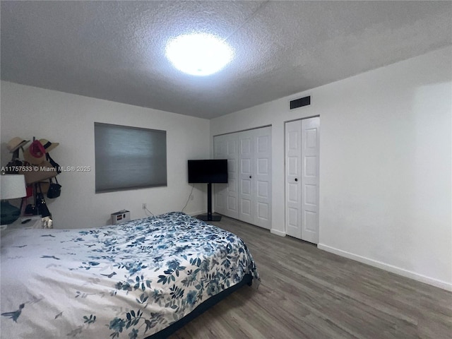 bedroom featuring a textured ceiling, wood finished floors, visible vents, baseboards, and multiple closets