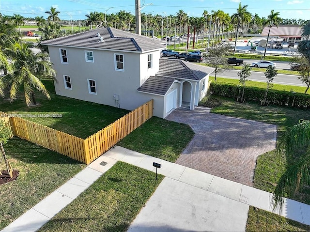 exterior space featuring an attached garage, fence private yard, a yard, decorative driveway, and stucco siding