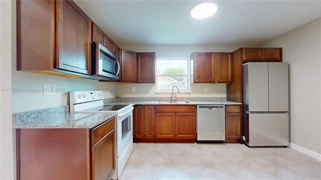 kitchen with light stone countertops, baseboards, a sink, appliances with stainless steel finishes, and brown cabinets