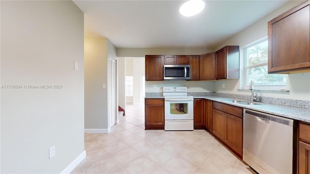 kitchen with brown cabinetry, stainless steel appliances, baseboards, and a sink