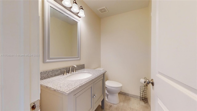 half bath featuring vanity, wood finished floors, baseboards, visible vents, and toilet