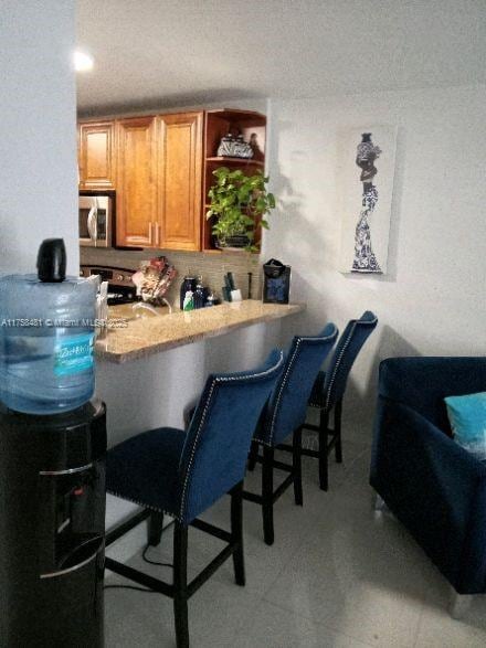 kitchen with stainless steel appliances, brown cabinetry, a kitchen breakfast bar, and open shelves