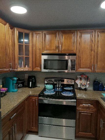 kitchen with light stone counters, appliances with stainless steel finishes, glass insert cabinets, and tasteful backsplash