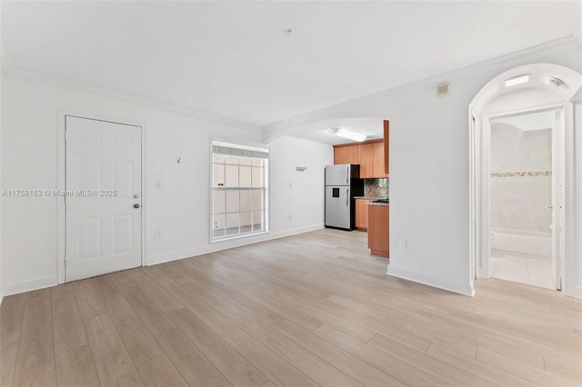 unfurnished living room with ornamental molding, light wood-type flooring, and baseboards