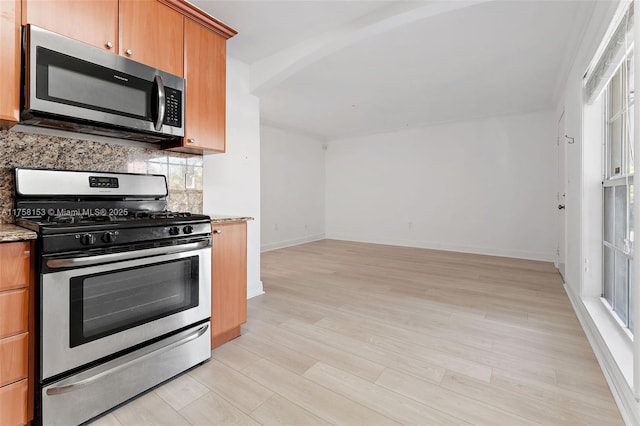 kitchen with light stone counters, tasteful backsplash, appliances with stainless steel finishes, light wood-type flooring, and baseboards