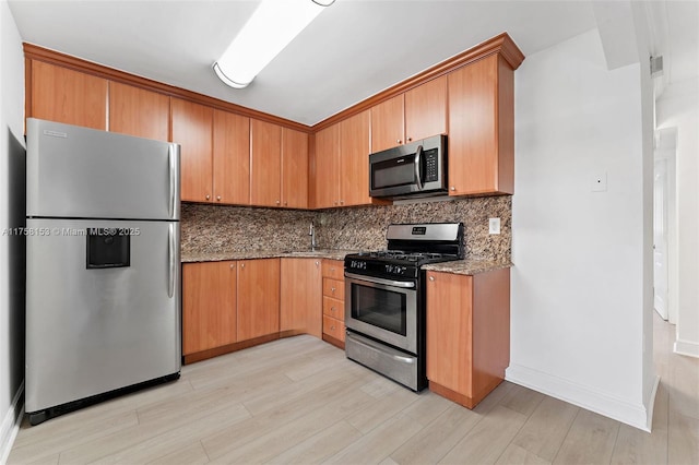 kitchen with stone countertops, baseboards, stainless steel appliances, light wood-style floors, and backsplash