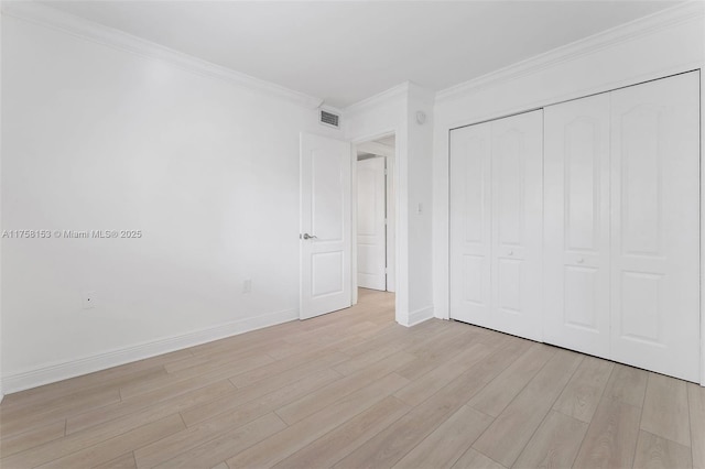 unfurnished bedroom with crown molding, light wood finished floors, a closet, visible vents, and baseboards