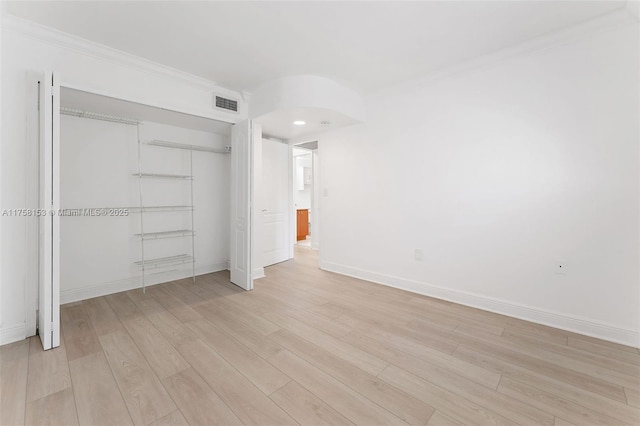 unfurnished bedroom with arched walkways, a closet, visible vents, light wood-style floors, and baseboards