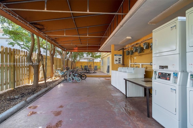 view of patio / terrace featuring outdoor dining area, washing machine and clothes dryer, fence, stacked washing maching and dryer, and exterior kitchen