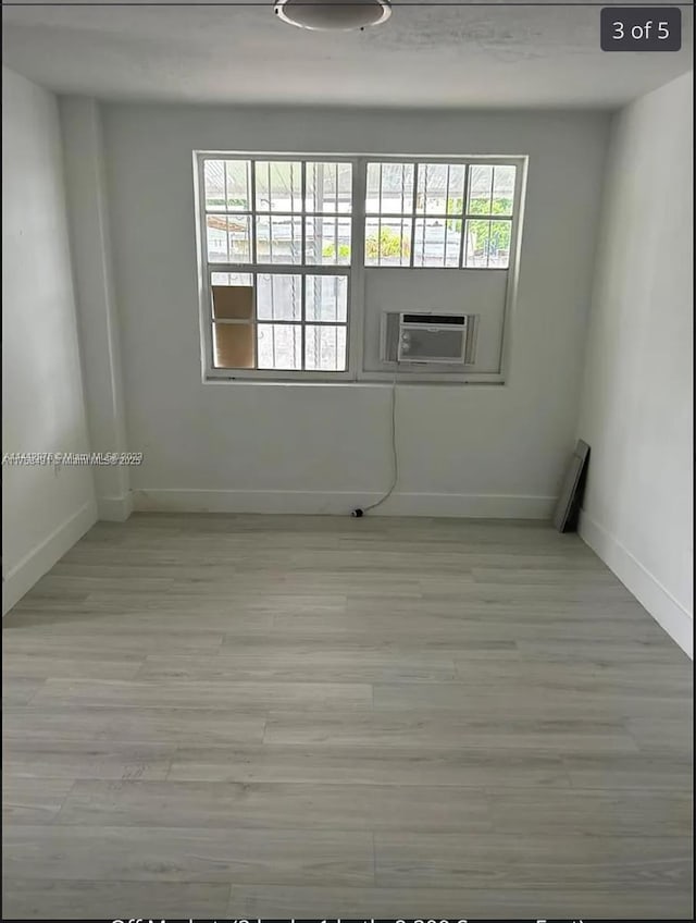 empty room featuring light wood-style floors, baseboards, and cooling unit