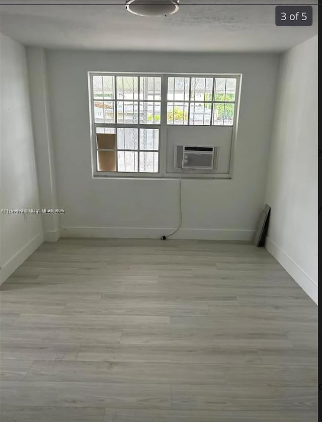 unfurnished room with light wood-type flooring, baseboards, and cooling unit