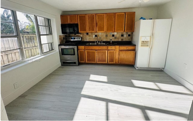 kitchen with white refrigerator with ice dispenser, black microwave, brown cabinetry, and stainless steel range with electric cooktop