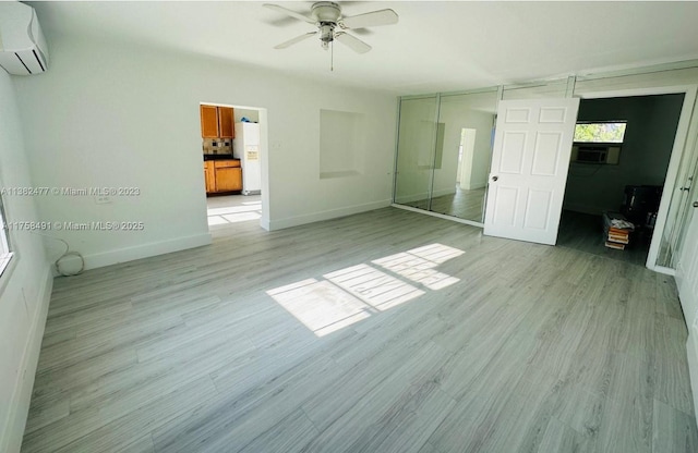 unfurnished bedroom featuring cooling unit, baseboards, a wall mounted air conditioner, and light wood finished floors