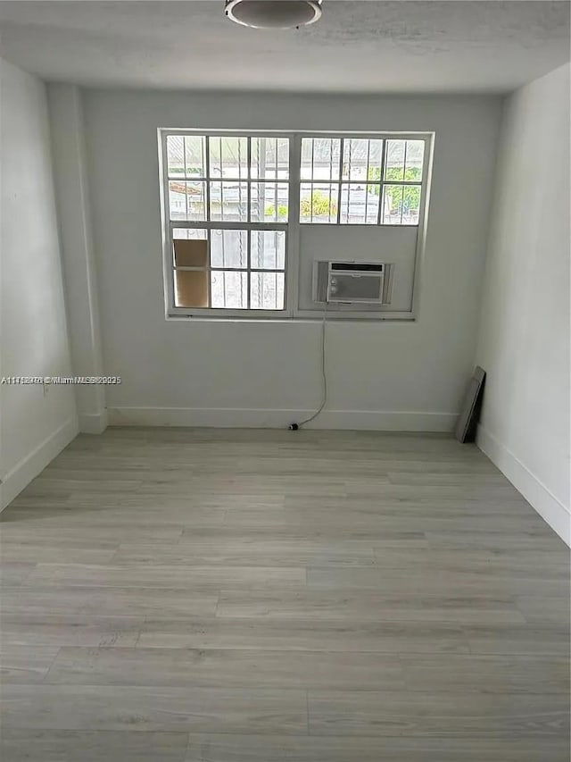 empty room featuring cooling unit, baseboards, and wood finished floors