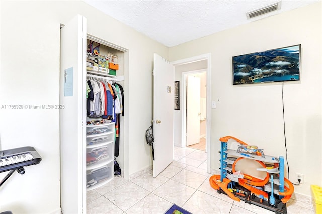 interior space featuring a closet, visible vents, a textured ceiling, and light tile patterned floors