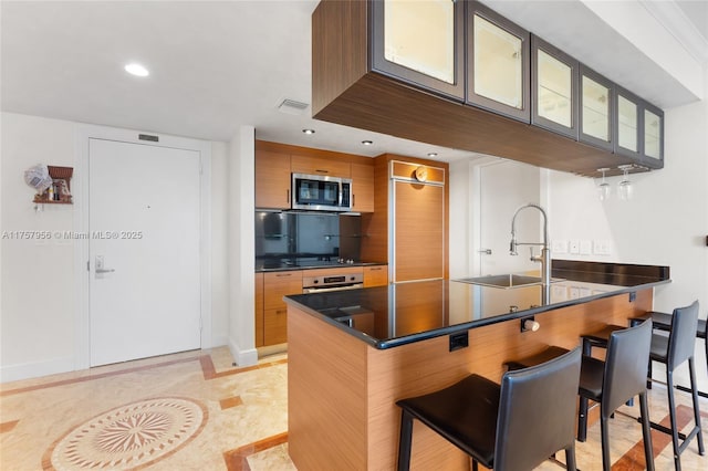 kitchen featuring visible vents, a breakfast bar area, stainless steel microwave, a peninsula, and a sink