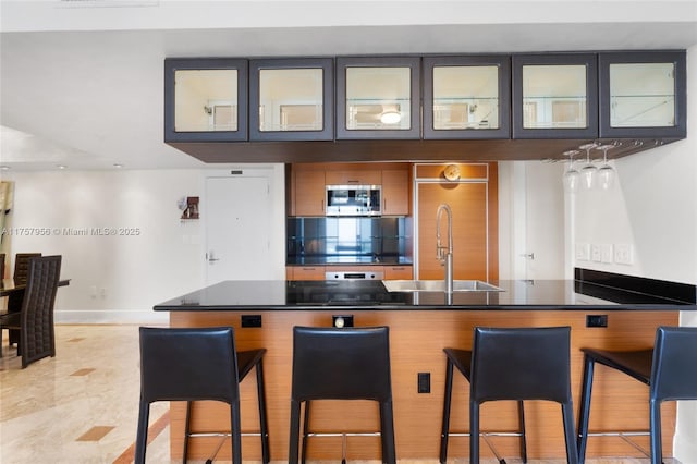 kitchen featuring a sink, dark countertops, stainless steel microwave, and a breakfast bar area