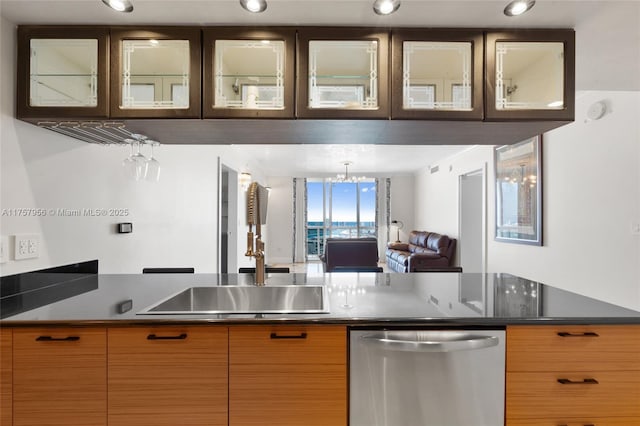 kitchen featuring dark countertops, stainless steel dishwasher, glass insert cabinets, open floor plan, and a sink