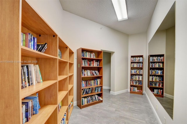 living area with bookshelves, a textured ceiling, and baseboards
