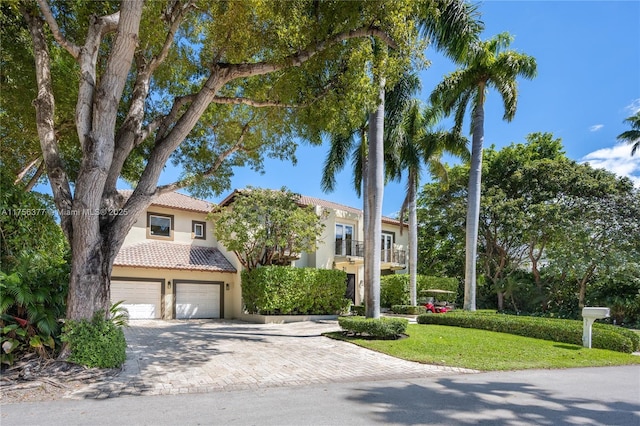 view of front of home with decorative driveway, stucco siding, an attached garage, a tiled roof, and a front lawn