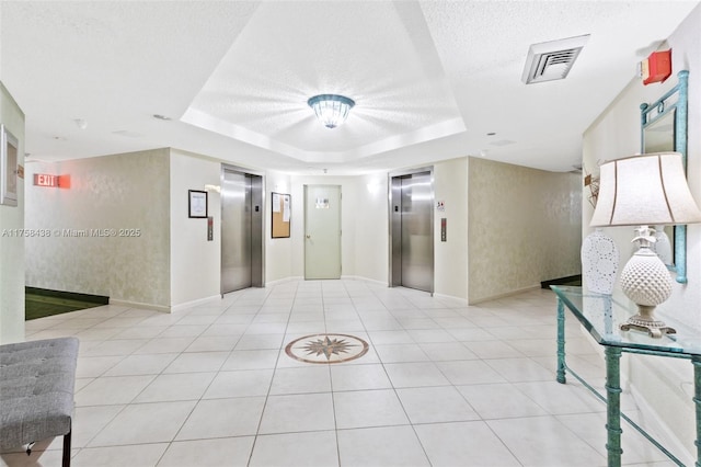 hallway with a tray ceiling, elevator, visible vents, and a textured ceiling