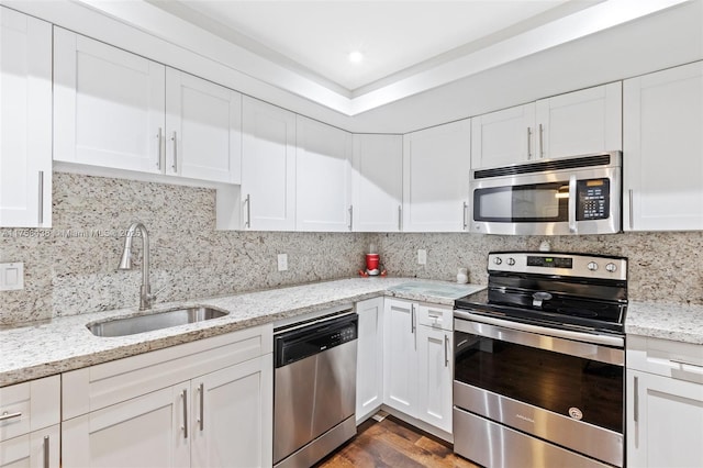 kitchen with appliances with stainless steel finishes, white cabinets, a sink, and backsplash