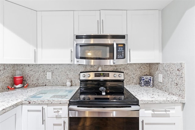 kitchen with light stone countertops, appliances with stainless steel finishes, white cabinets, and decorative backsplash