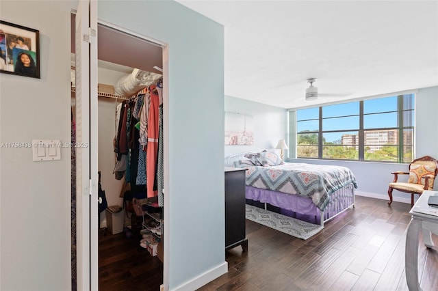 bedroom with dark wood-type flooring, a walk in closet, a closet, and baseboards