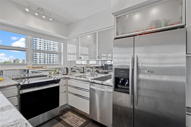 kitchen with light stone countertops, appliances with stainless steel finishes, white cabinets, a sink, and modern cabinets