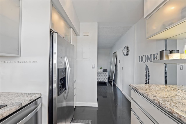 kitchen with stainless steel fridge with ice dispenser, glass insert cabinets, light stone countertops, dark tile patterned floors, and baseboards