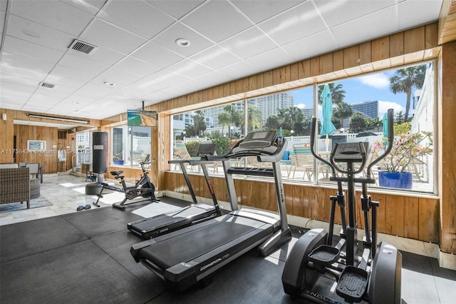 workout area featuring a healthy amount of sunlight, wood walls, visible vents, and a drop ceiling