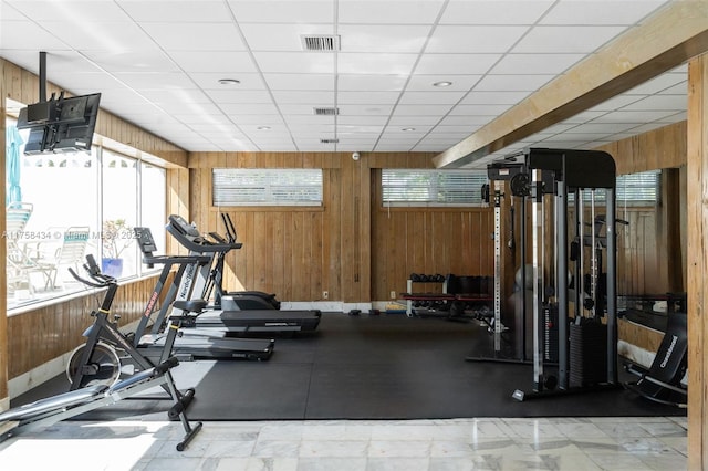 exercise room featuring a paneled ceiling, visible vents, and wooden walls