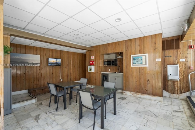 dining space featuring marble finish floor, a drop ceiling, and wood walls