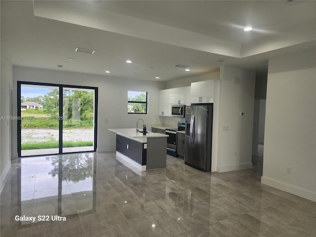 kitchen featuring a kitchen island with sink, a sink, baseboards, light countertops, and appliances with stainless steel finishes