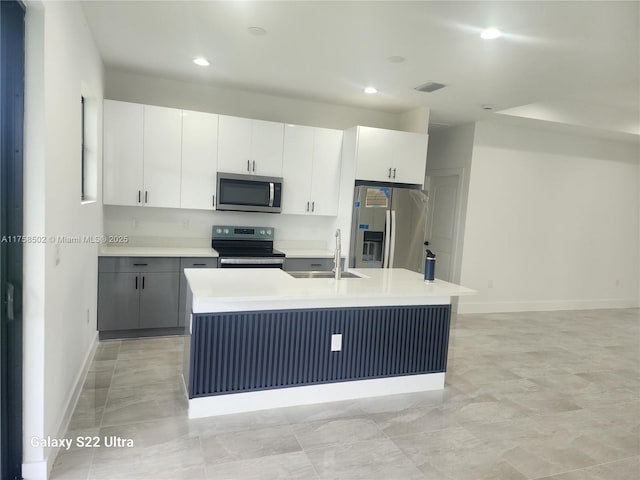 kitchen with visible vents, appliances with stainless steel finishes, a kitchen island with sink, light countertops, and a sink