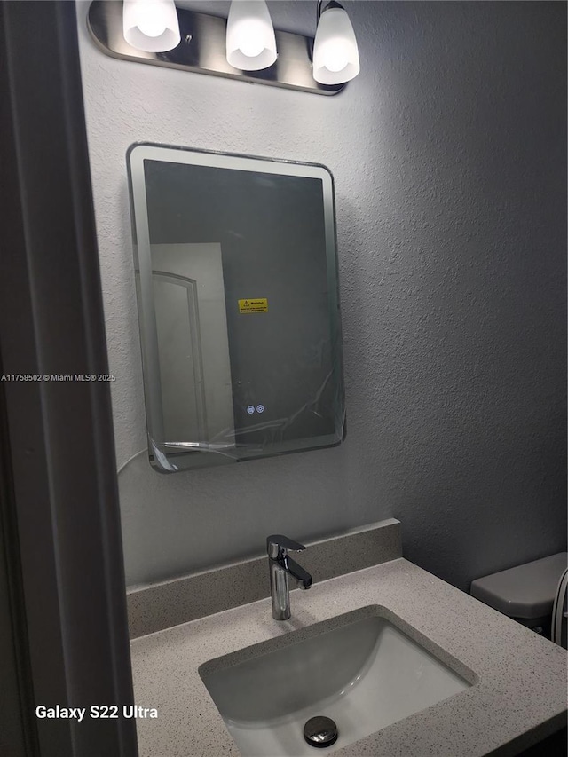 bathroom featuring toilet, a textured wall, and vanity