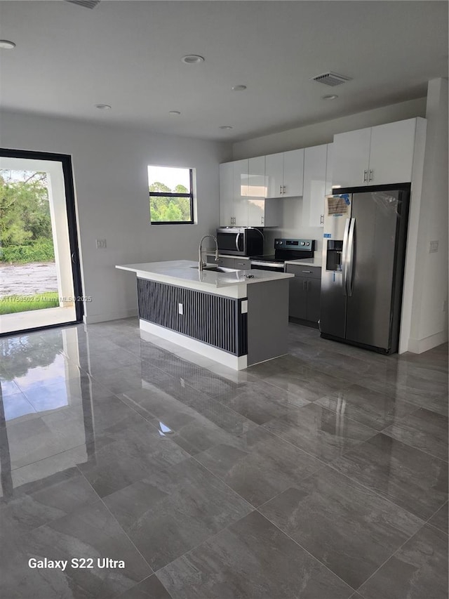 kitchen with white cabinets, a kitchen island with sink, stainless steel appliances, and light countertops