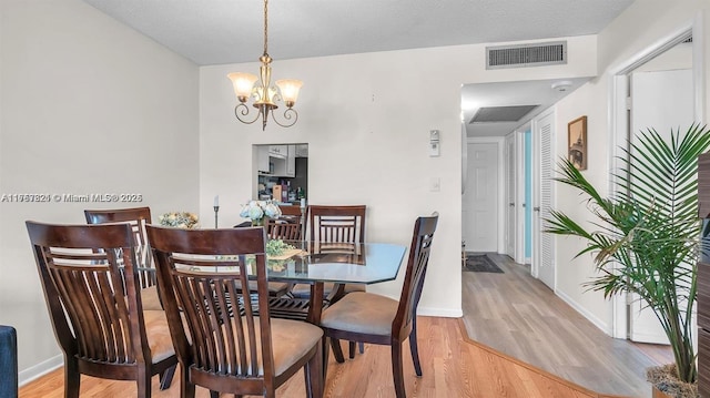 dining room featuring light wood-style floors, baseboards, visible vents, and an inviting chandelier