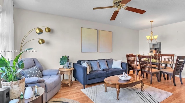 living area featuring ceiling fan with notable chandelier, a textured ceiling, and light wood-style flooring