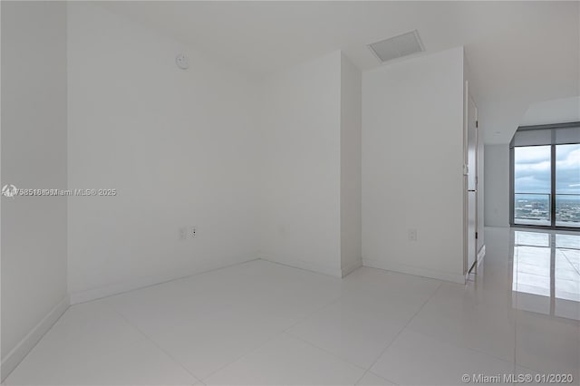 spare room featuring floor to ceiling windows, tile patterned floors, visible vents, and baseboards