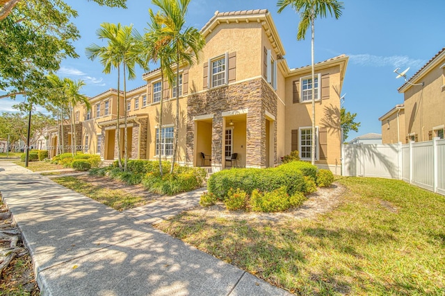 view of front of house featuring fence, stone siding, a residential view, stucco siding, and a front lawn